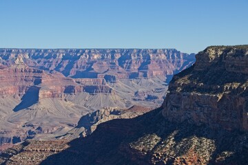 Bright desert sunlight shines down on the Grand Canyon, casting shadows on every crease and layer of the eroded canyon carved over many years by the Colorado River thousands of feet below