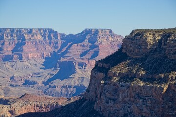 Bright desert sunlight shines down on the Grand Canyon, casting shadows on every crease and layer of the eroded canyon carved over many years by the Colorado River thousands of feet below
