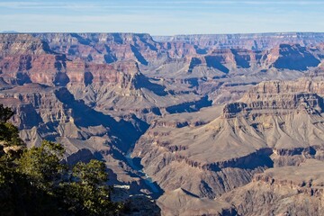 Fototapeta na wymiar Bright desert sunlight shines down on the Grand Canyon, casting shadows on every crease and layer of the eroded canyon carved over many years by the Colorado River thousands of feet below