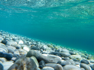 Fototapeta na wymiar UNDERWATER sea level photo. Turquoise crystal clear water, pebbles of Agia Kyriaki beach in Kyparissi Laconia, Greece.
