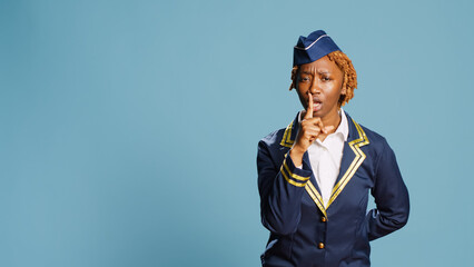 African american girl doing mute silent gesture in studio, acting confidential and keeping secret. Young aircrew member dressed in uniform being private and asking for secrecy with hush sign.