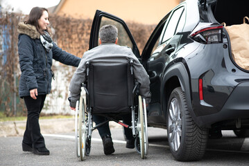 Obraz premium A woman helps aphysical disabled person to get into the car