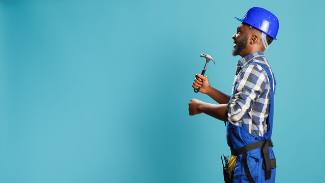 African american carpenter hitting walls with hammer, using manual instrument for renovation and reconstruction work. Male constructor in overalls holding jackhammer mullet tool.
