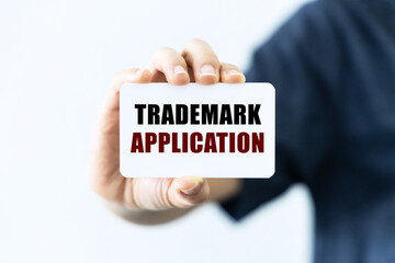 Trademark application text on blank business card being held by a woman's hand with blurred...