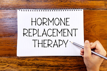 Hormone replacement therapy handwriting text on blank notebook paper on wooden table with hand holding pencil. Business concept about hormone therapy. - obrazy, fototapety, plakaty