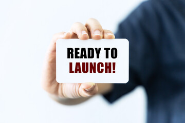 Ready to launch text on blank business card being held by a woman's hand with blurred background. Business concept about launching product.