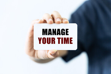 Manage your time text on blank business card being held by a woman's hand with blurred background. Business concept about time management.