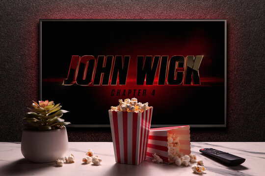 TV screen playing John Wick Chapter 4 trailer or movie. TV with remote control, popcorn boxes and home plant. Moscow, Russia - March 23, 2023.