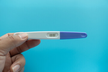 Young woman hand holding positive pregnancy test result with two stripes on pastel blue background. Closeup. Point of view shot. Top down view. Empty place for text.