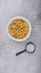 instant noodles with magnifying glass in the bowl on cement texture background