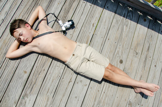 Young preteen boy laying on sunny boardwalk with camera