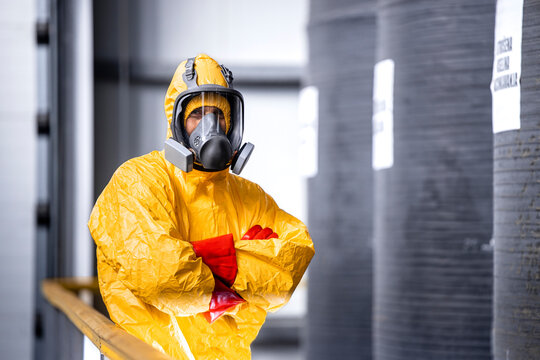 Portrait of factory worker in protective yellow suit, gas mask and gloves standing inside chemicals plant by the acid tanks.