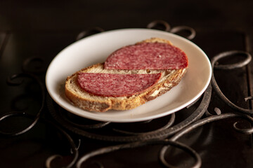 Bread with salami on a white plate on a dark background. Simple sandwich.