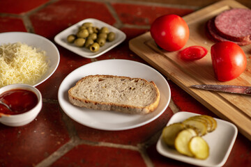 Sandwich preparation. A piece of bread on a plate surrounded by various ingredients.