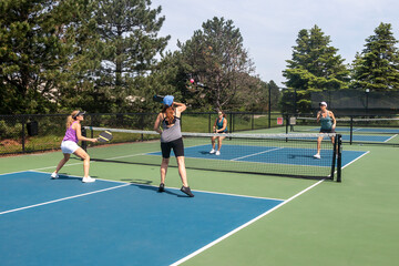 Two players approach the net in a competitive doubles game of pickleball on a blue and green court...