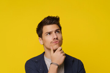 Close up of young man on yellow background, with facial expression conveying confusion and...