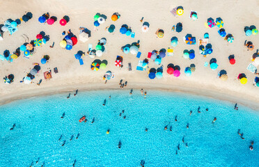 Aerial view of colorful umbrellas on beach, people in blue sea