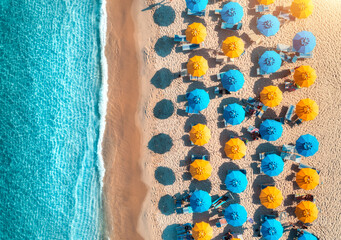 Aerial view of yellow and blue umbrellas on empty sandy beach