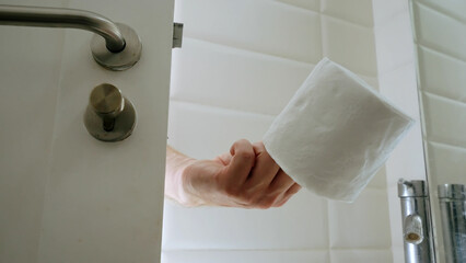 Man hand behind door holding new toilet paper. Returning finished toilet paper