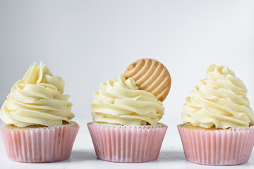 Pink cupcakes with tall american buttercream swirl and cookie garnish, cupcakes in pink liners with a tall vanilla buttercream and a cookie, birthday cupcakes on a white background