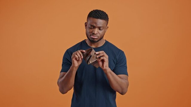 Sad African American man expressing sadness and despair at camera, showing his empty leather wallet