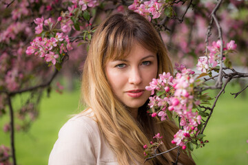 Spring portrait of a beautiful caucasian woman standing beside a tree in bloom. She has blonde hair and blue eyes. She is at a local park. 