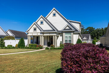 Fototapeta na wymiar The front view of a cottage craftsman style white house with a triple pitched roof with a sidewalk, landscaping and curb appeal