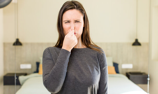young adult pretty woman feeling disgusted, holding nose to avoid smelling a foul and unpleasant stench