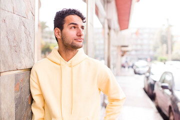 young hispanic man wondering, thinking happy thoughts and ideas, daydreaming, looking to copy space on side