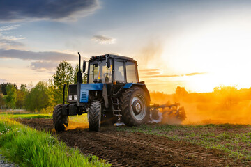 Modern blue tractor machinery plowing agricultural field meadow at farm at spring autumn during...