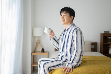 朝、ベッドでコーヒーを飲む50代男性