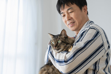 ベッドに座って猫を抱くパジャマ姿の50代男性