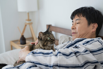 目が覚めてベッドで猫と戯れる50代男性