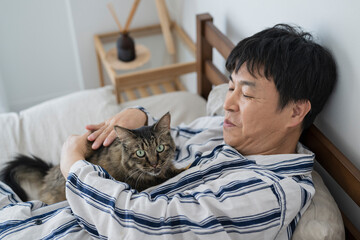 目が覚めてベッドで猫と戯れる50代男性