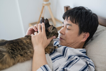 目が覚めてベッドで猫と戯れる50代男性