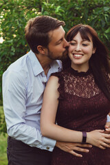 Fototapeta premium Outdoor portrait of a caucasian couple embracing in the summer at a park. The man is kissing the woman's cheek and the woman is smiling. T