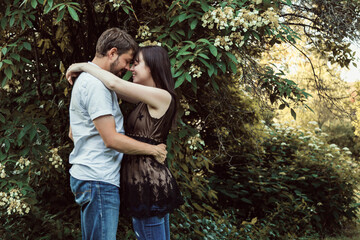 Portrait of a caucasian couple embracing at at park. There is empty space to the right. The couple is in their 30s. 