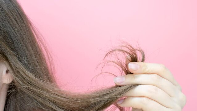 Girl holding her hair with split ends close-up on pink background.