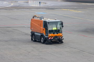 A small cleaning truck with brooms drives on the runway