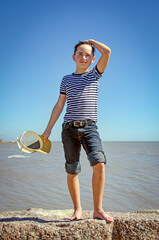 Young preteen boy standing on sunny beach wearing jeans and hat