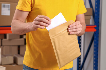 Post office worker putting envelope into adhesive bag indoors, closeup
