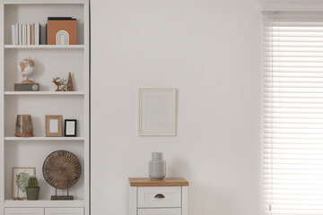 Stylish shelves with different decor elements and chest of drawers in room. Interior design