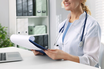Doctor with laptop and clipboard at white table in clinic, closeup. Patient consultation