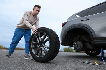 Fototapeta na wymiar Young man changing tire of car on roadside