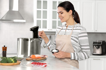 Woman salting products near pot with sous vide cooker at table in kitchen. Thermal immersion...