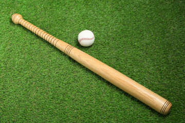 Fototapeta na wymiar Wooden baseball bat and ball on green grass, above view. Sports equipment