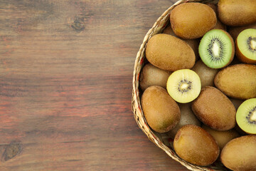 Basket of many whole and cut fresh kiwis on wooden table, top view. Space for text