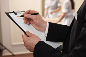 Man wearing suit with clipboard checking maid's work in hotel room, closeup. Professional butler...
