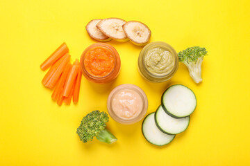 Glass jars with healthy baby food and ingredients on yellow background, flat lay