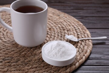 Bowl of fructose powder and cup with tea on dark wooden table